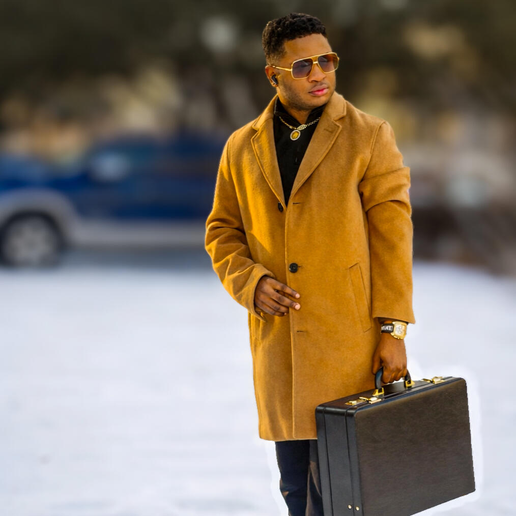 Nate Haliv wearing a camel coat and carrying a black briefcase.